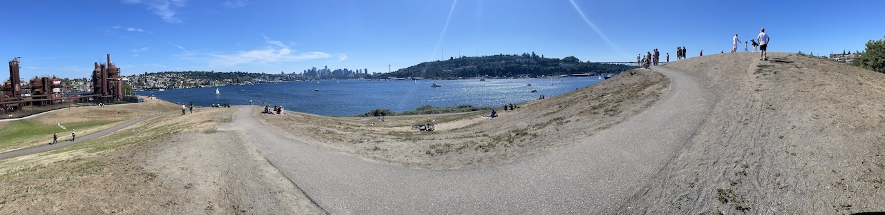 a panorama image of gasworks park, looking south over south lake union. the day is sunny, the lake is calm, and the path lays at your feet