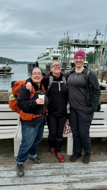 Three women stand in height order, shortest to tallest, with about a foot between the ranges. All three are grinning in front of a ferry.
